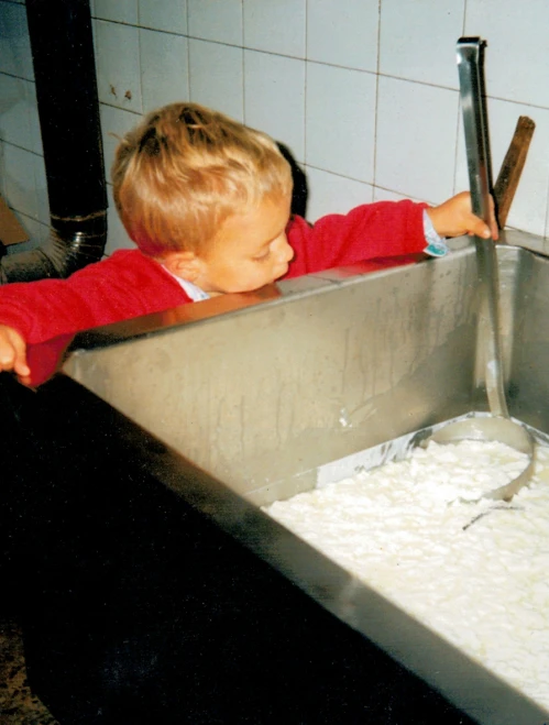 Niño observando la tina de leche y cuajada en la quesería de Tresviso, aprendiendo desde pequeño.